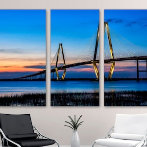 May include: A panoramic view of a bridge at dusk. The bridge is a cable-stayed bridge with a large central span and two smaller side spans. The bridge is lit up with golden lights, and the sky is a deep blue with a hint of pink and orange. The water below the bridge is calm and reflective.