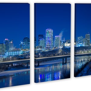 May include: A triptych canvas print of a city skyline at night. The buildings are illuminated with various colors, reflecting in the water below. A bridge with car lights crosses the river. The sky is a deep blue.