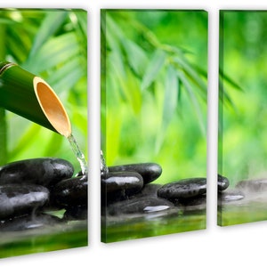 May include: A bamboo fountain with water flowing over smooth black stones. The water creates a mist as it flows into a pool of water. The background is a blurred image of green bamboo leaves.
