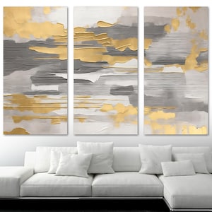 May include: Abstract wall art set of three panels. The artwork features gold, gray, and white textured paint. The gold paint has a metallic sheen, and the gray paint has horizontal brushstrokes. The panels are rectangular and mounted above a white sofa.