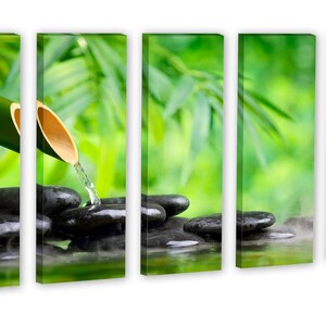 May include: A bamboo shoot with water flowing from it onto smooth black stones in a pool of water. The background is a blurred image of green leaves.