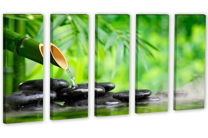 May include: A bamboo shoot with water flowing from it onto smooth black stones in a pool of water. The background is a blurred image of green leaves.
