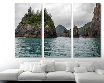 May include: A panoramic view of a rocky, green island with a forested top, surrounded by calm, blue water. The island is part of a group of islands, all with similar features. The sky is overcast and grey.