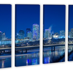 May include: A four-panel canvas print of a city skyline at night. Buildings with illuminated windows and lights are reflected in the water below. The sky is a deep blue, and the scene evokes a sense of urban life.