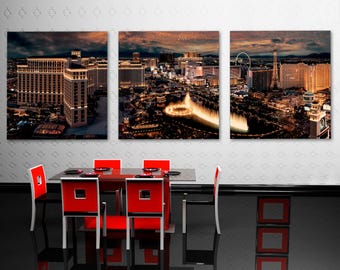 May include: A triptych of canvas prints depicting the Las Vegas skyline at night. The prints show illuminated buildings, a fountain, and the Eiffel Tower. A modern dining table with red chairs is in the foreground.