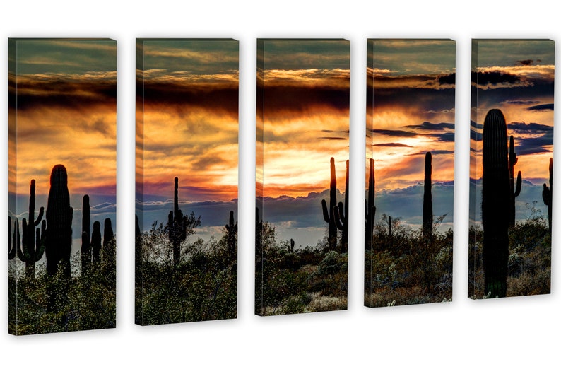 May include: A five-panel canvas print depicting a desert sunset. Silhouetted saguaro cacti stand in the foreground against a vibrant sky of orange, yellow, and purple hues. The artwork captures the serene beauty of the desert landscape.