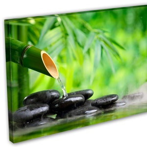 May include: A bamboo pipe pours water onto smooth black stones in a shallow pool. The water creates steam and the background is a blurred image of green bamboo leaves.