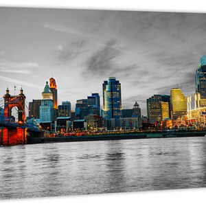 Pu&ograve; includere: Un paesaggio urbano in bianco e nero con un ponte rosso in primo piano. Lo skyline della citt&agrave; &egrave; illuminato da luci gialle calde. Il fiume in primo piano &egrave; calmo e riflettente.