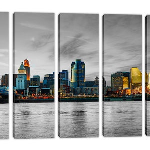Pu&ograve; includere: Una vista panoramica dello skyline di Cincinnati al tramonto, con l'iconico ponte sospeso Roebling, il Great American Ball Park e diversi grattacieli. La citt&agrave; &egrave; illuminata da luci calde che si riflettono nel fiume Ohio.