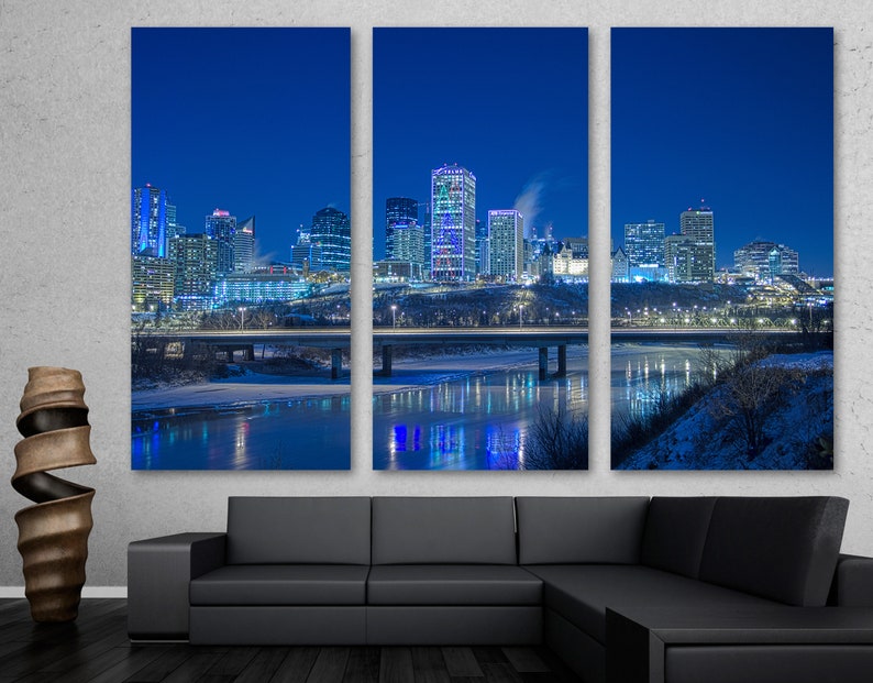 May include: A triptych canvas print featuring a nighttime cityscape with illuminated skyscrapers. The buildings are reflected in the water below, with a bridge in the foreground. The sky is a deep blue, and the overall scene is cold and wintry.