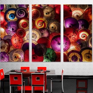 May include: A set of three colorful canvas prints featuring a close-up of a collection of Japanese umbrellas with various patterns and designs. The umbrellas are arranged in a circular pattern and are illuminated with warm lighting.