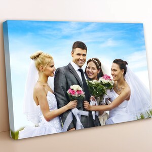 May include: A group of four people in wedding attire pose for a photo. The groom stands in the center, holding a bouquet of pink flowers. The two brides stand on either side of him, each holding a bouquet of white and pink flowers. The fourth person is a bridesmaid, standing behind the brides, with a white veil and a bouquet of pink and white flowers.