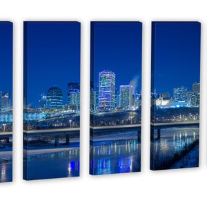 May include: A five-panel canvas print of a city skyline at night. The buildings are illuminated with various colors, reflecting in the water below. A bridge crosses the water, and the sky is a deep blue.