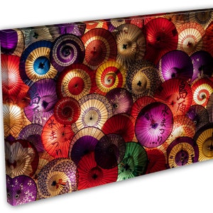 May include: A colorful display of Japanese paper umbrellas, or washi, hanging from the ceiling. The umbrellas are in various shades of red, pink, purple, blue, and yellow, with intricate designs and patterns. Some of the umbrellas have Japanese characters written on them.