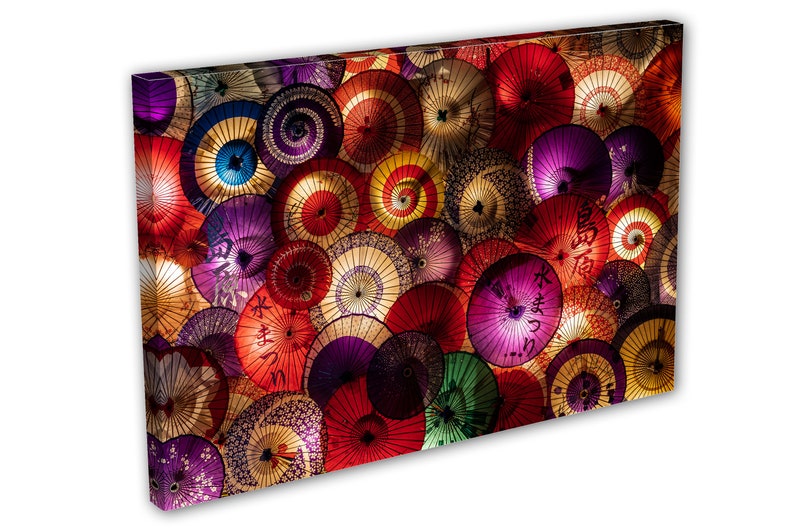 May include: A colorful display of Japanese paper umbrellas, or washi, hanging from the ceiling. The umbrellas are in various shades of red, pink, purple, blue, and yellow, with intricate designs and patterns. Some of the umbrellas have Japanese characters written on them.