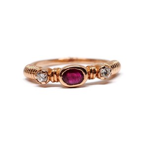 Puede incluir: Un anillo de oro rosa con un rubí rojo y dos pequeños diamantes.