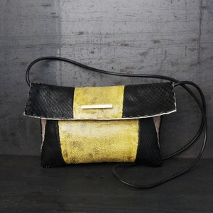 Könnte beinhalten: Eine schwarze und gelbe Leder-Umhängetasche mit Klappenverschluss. Die Tasche hat eine strukturierte, abgenutzte Optik.