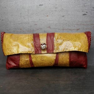 Könnte beinhalten: Eine gelbe und rote Lederclutch mit einem silbernen Verschluss. Die Clutch hat eine strukturierte Oberfläche und einen Klappverschluss.