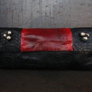May include: A black and red leather clutch with silver embellishments. The clutch has a textured surface and a flap closure.