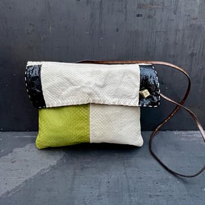 May include: A handmade clutch purse with a brown leather strap. The purse features a color block design with sections of white, black, and green textured leather. The strap is attached with small gold-colored rivets.