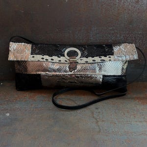 May include: A black, white and silver snakeskin clutch bag with a silver ring closure and a black strap.