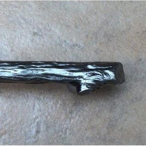 May include: A dark gray, twig-shaped cabinet pull. The hardware has a textured surface, mimicking the look of tree bark. The pull is designed to be mounted horizontally and has a rustic, natural aesthetic.