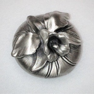 May include: A silver metal flower ornament with a detailed design. The flower is a stylized orchid with petals and leaves.