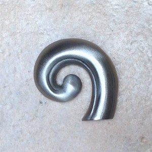 May include: A silver metal decorative scroll with a spiral design.