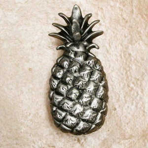 May include: A silver pineapple-shaped door knob or pull. The pineapple is detailed with a textured surface and a leafy top.