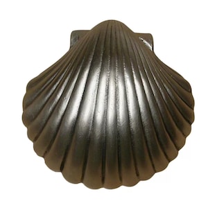 May include: A dark gray, cast metal seashell with a textured surface. The shell has a fan-like shape with detailed ridges radiating from the center. The back has a rectangular mounting feature. The overall design is reminiscent of coastal decor.