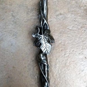 May include: A silver-colored metal bottle stopper with a nature-inspired design. The stopper features a central stem with a detailed leaf and vine motif. The design is intricate and adds a touch of elegance to any bottle.