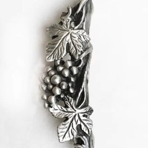May include: A silver-toned metal grapevine pendant with a cluster of grapes and leaves. The pendant is detailed and realistic.