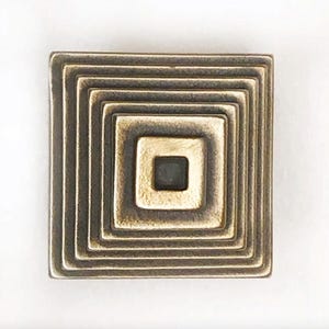 May include: A square-shaped brass ornament with concentric squares, each with a slightly raised edge. The innermost square is the smallest and has a slightly darker finish.