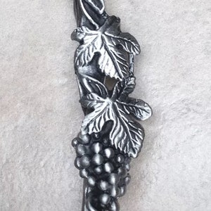 May include: A silver-toned metal grapevine design bottle stopper with a cluster of grapes and leaves.