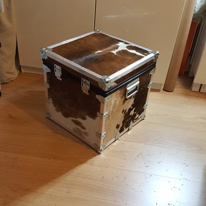 May include: A square storage trunk with a brown and white cowhide pattern. The trunk has silver metal accents and hinges.