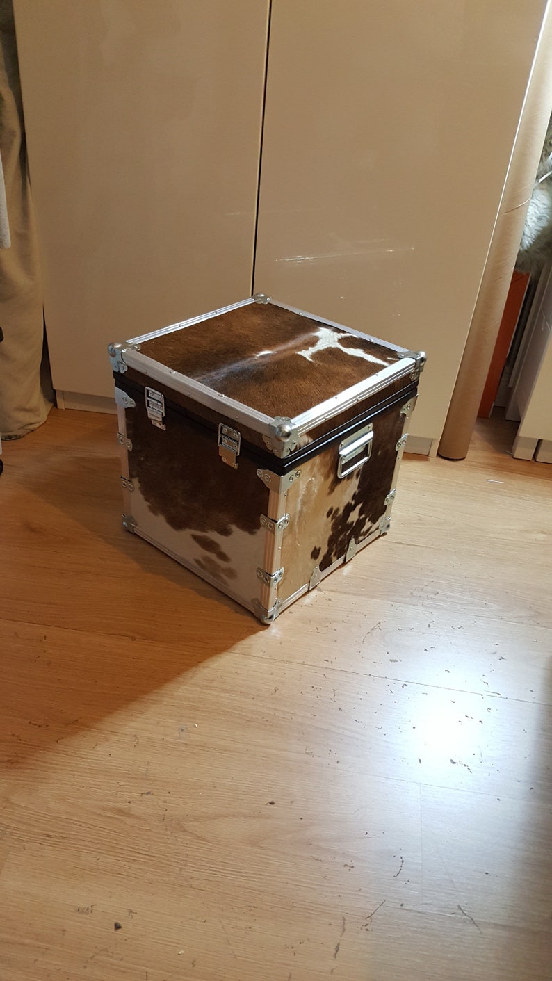 May include: A square storage trunk with a brown and white cowhide pattern. The trunk has silver metal accents and hinges.