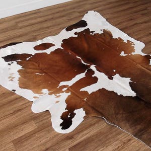 May include: A brown and white cowhide rug with a natural, irregular shape. The rug has a soft, plush texture and is perfect for adding a touch of rustic charm to any room.