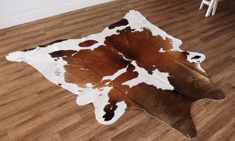May include: A brown and white cowhide rug with a natural, irregular shape. The rug has a soft, plush texture and is perfect for adding a touch of rustic charm to any room.