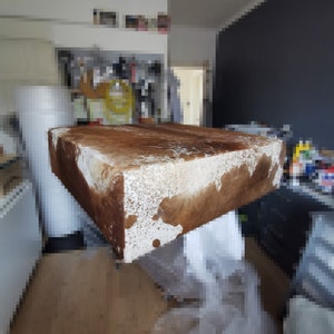K&ouml;nnte beinhalten: Ein rechteckiger Hocker aus braunem und wei&szlig;em Kuhfell. Der Hocker steht auf einem Holzboden.