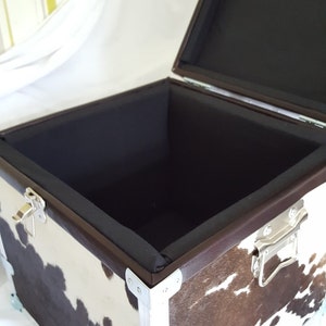 May include: A brown and white cowhide storage box with silver metal corners and a black fabric lining. The box is open and empty.