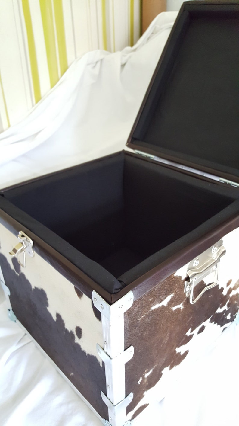 May include: A brown and white cowhide storage box with silver metal corners and a black fabric lining. The box is open and empty.