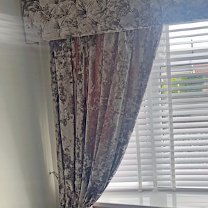 May include: A set of gray velvet curtains with a tufted valance. The curtains are hung on a window with white blinds.