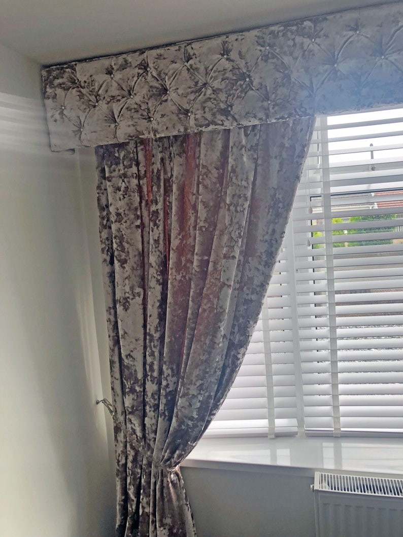 May include: A set of gray velvet curtains with a tufted valance. The curtains are hung on a window with white blinds.