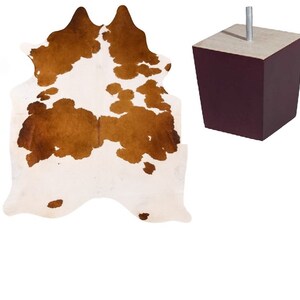 May include: A brown and white cowhide rug with a dark brown furniture leg.
