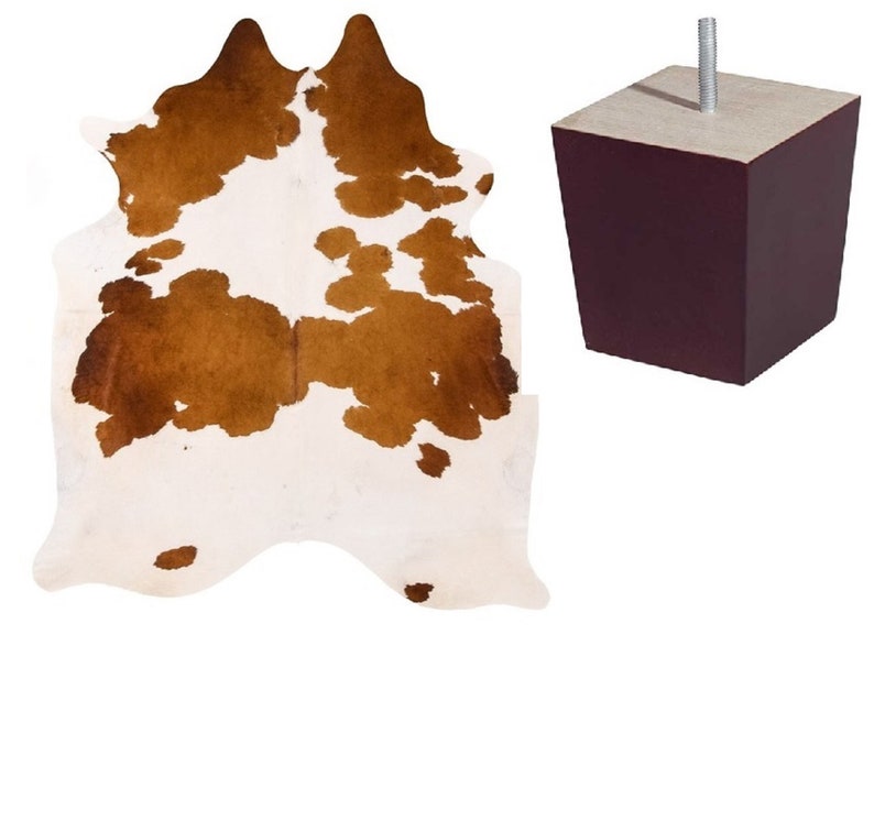 May include: A brown and white cowhide rug with a dark brown furniture leg.