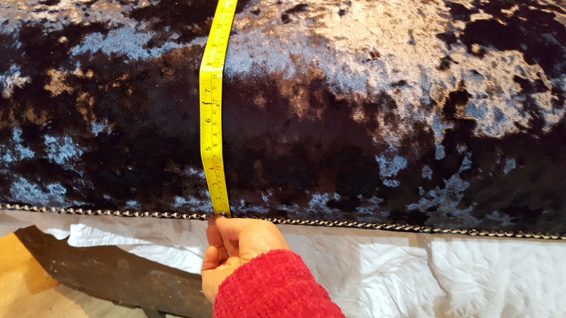 May include: Close-up of a dark blue velvet cushion with a silver and black pattern. A yellow measuring tape is being used to measure the length of the cushion, which is 17 inches.