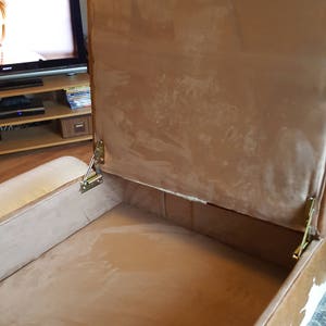 May include: A brown and white cowhide storage ottoman with a hinged lid. The lid is open, revealing a brown fabric interior.