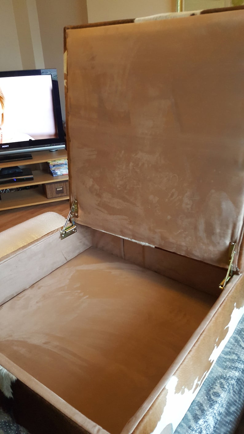 May include: A brown and white cowhide storage ottoman with a hinged lid. The lid is open, revealing a brown fabric interior.
