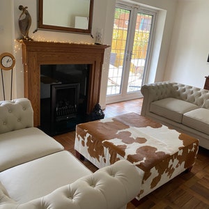 May include: A living room with two white sofas, a brown and white cowhide ottoman, a fireplace, and a flat screen TV.