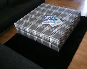 May include: A grey and white plaid ottoman with two books on top. The ottoman is sitting on a black rug.